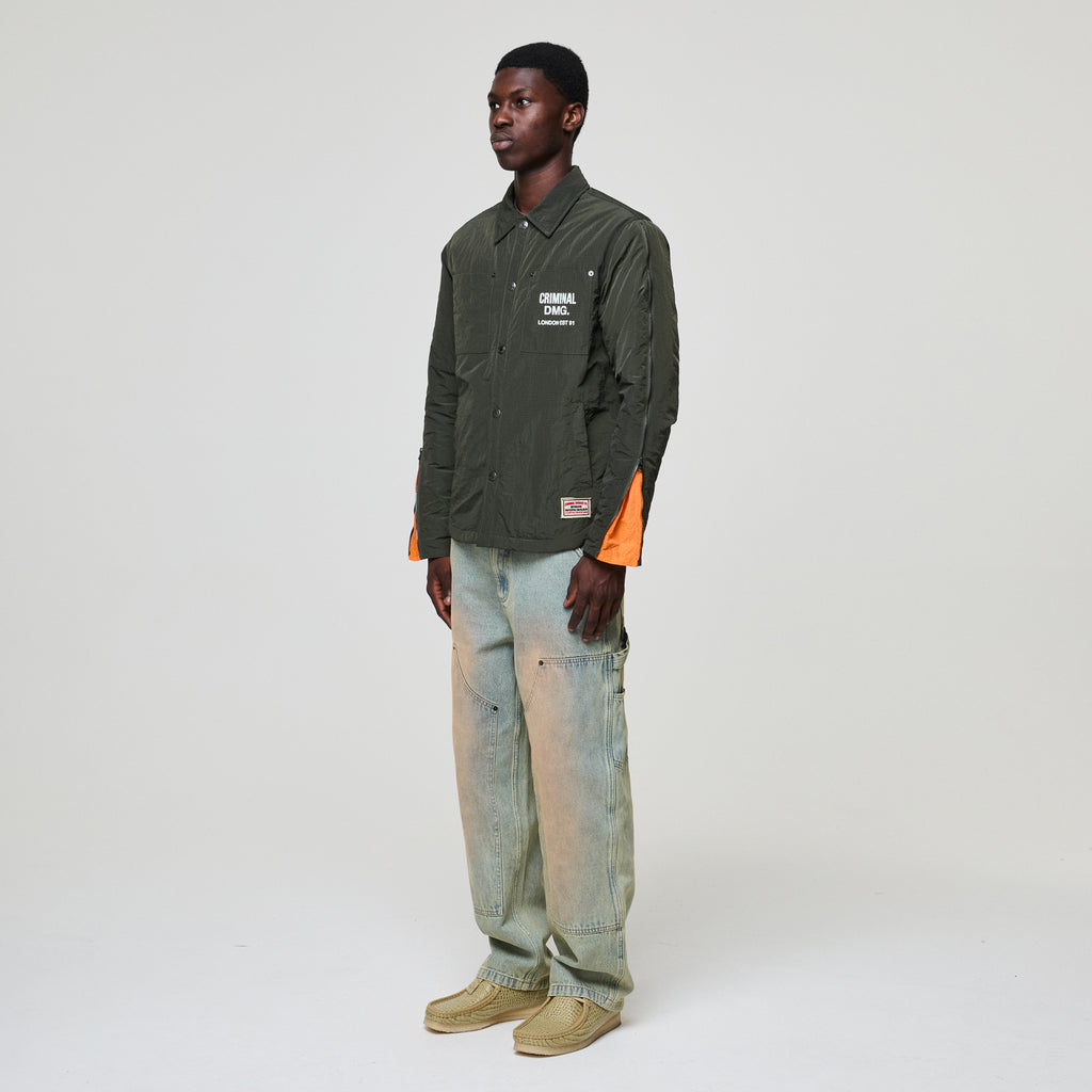 Person wearing a green Criminal Damage jacket and light blue jeans on a white background
