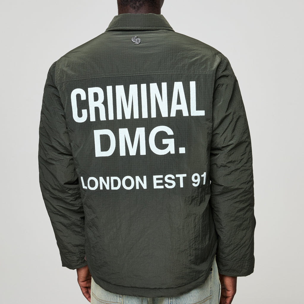 Person wearing a green jacket with Criminal Damage text on the back against a gray background