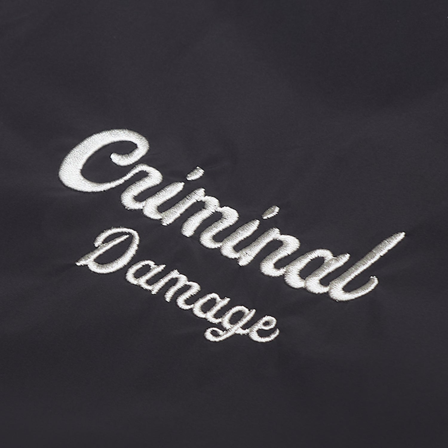Embroidered text 'Criminal Damage' on a dark background