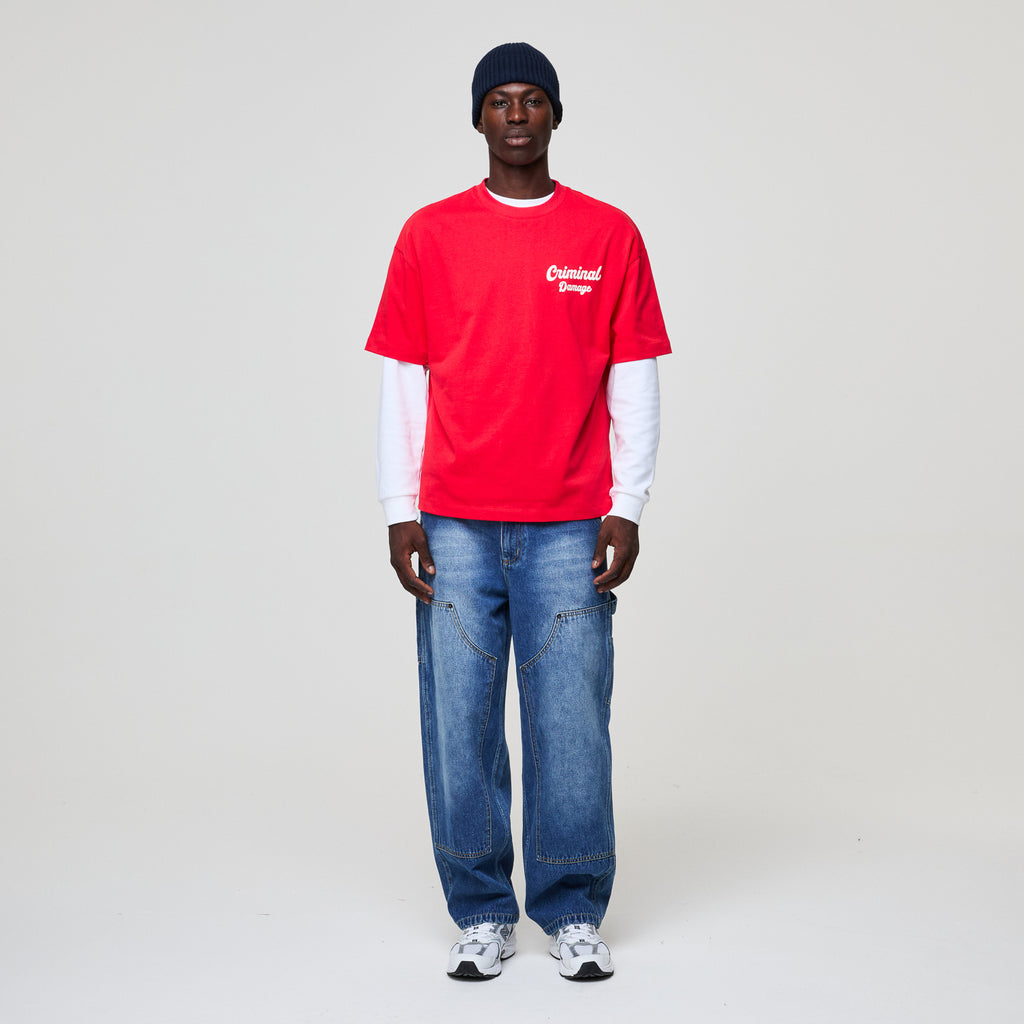 Person wearing a red shirt with a logo, blue jeans, and a black beanie on a white background