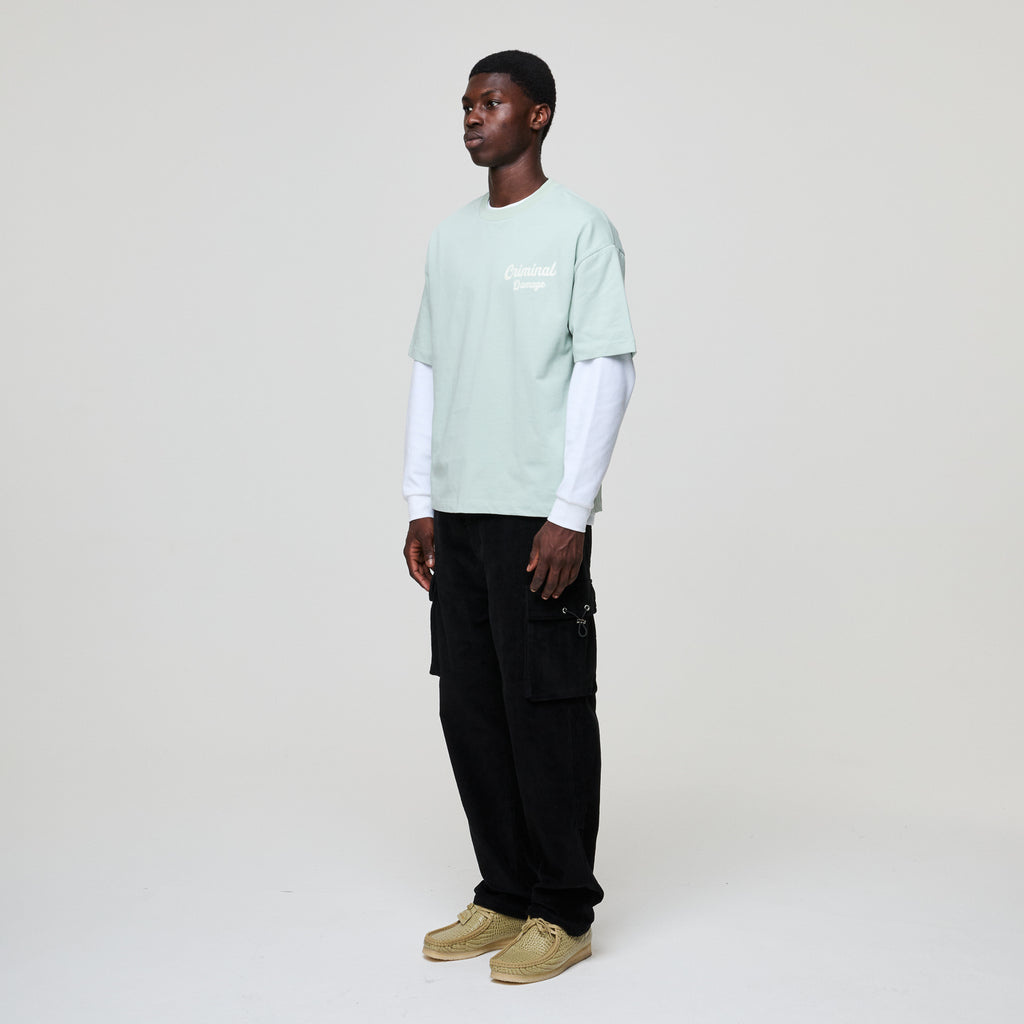 Person wearing a light green t-shirt, black pants, and beige shoes on a white background