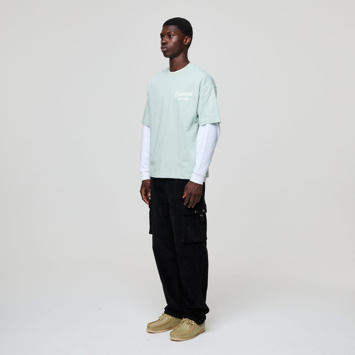 Person wearing a light green t-shirt, black pants, and beige shoes on a white background