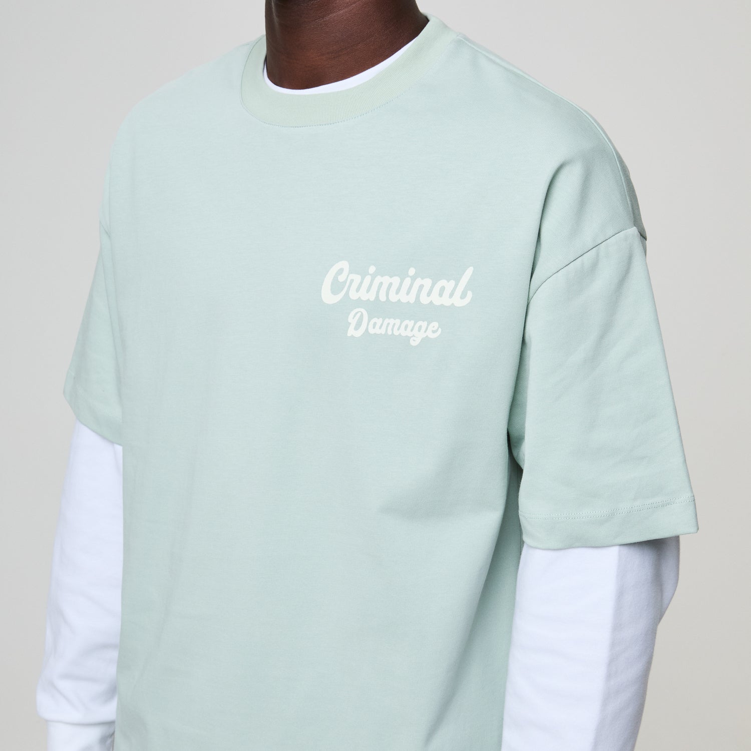 Light green t-shirt with 'Criminal Damage' text on a plain background