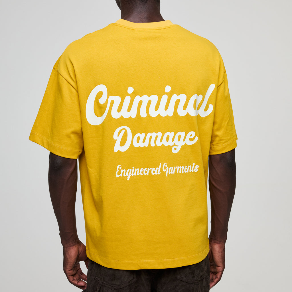 Yellow t-shirt with 'Criminal Damage' text on a plain background