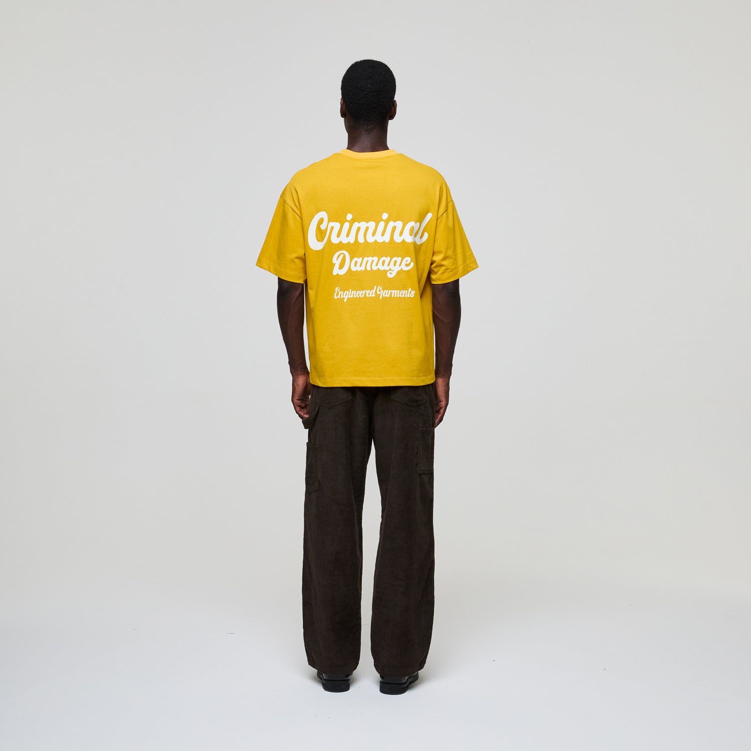 Person wearing a yellow 'Criminal Damage' t-shirt on a white background