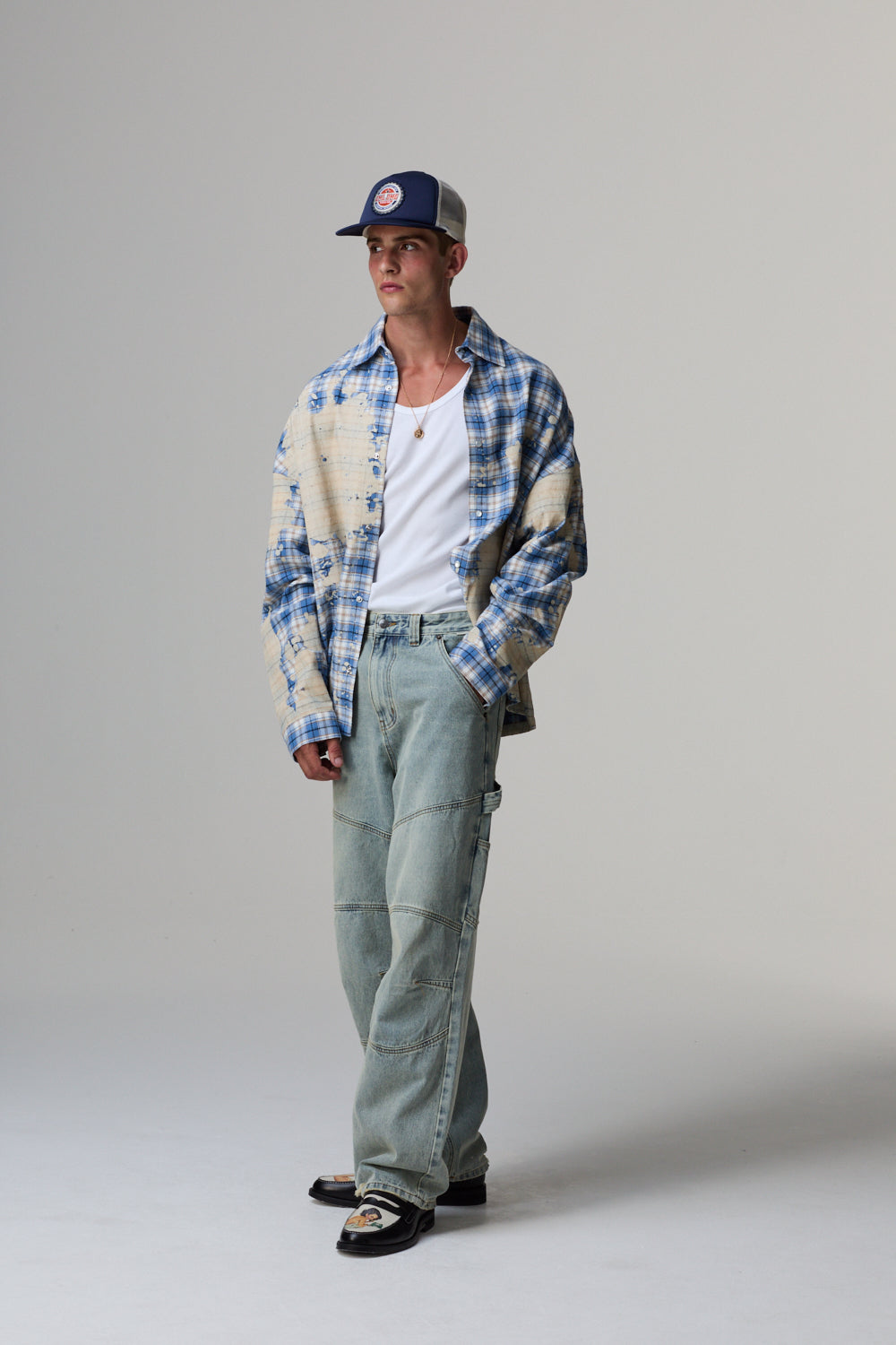 Man wearing a plaid shirt, cap, and jeans on a grey background