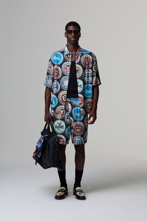Model wearing a colourful Criminal Damage patterned shirt and shorts with a black bag on a grey background