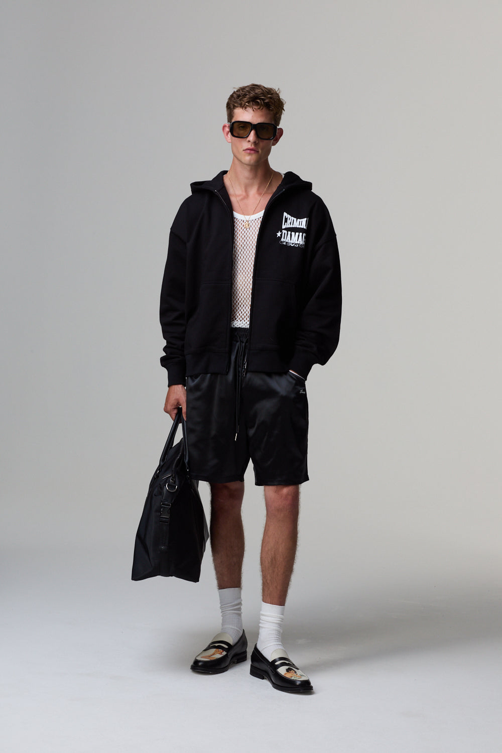 Model wearing a black Criminal Damage hoodie and shorts with sunglasses on a grey background
