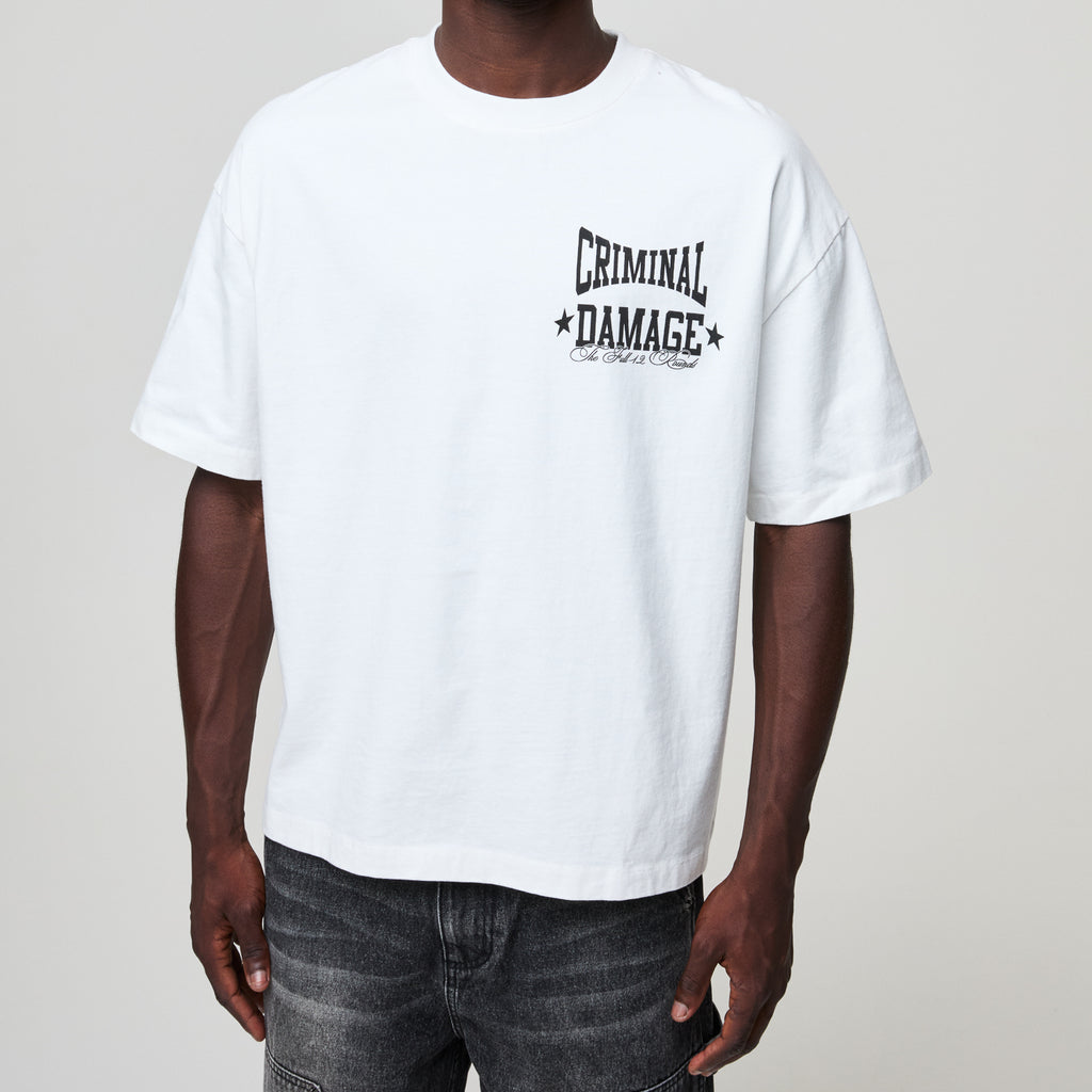 Person wearing a white t-shirt with 'Criminal Damage' print on a plain background