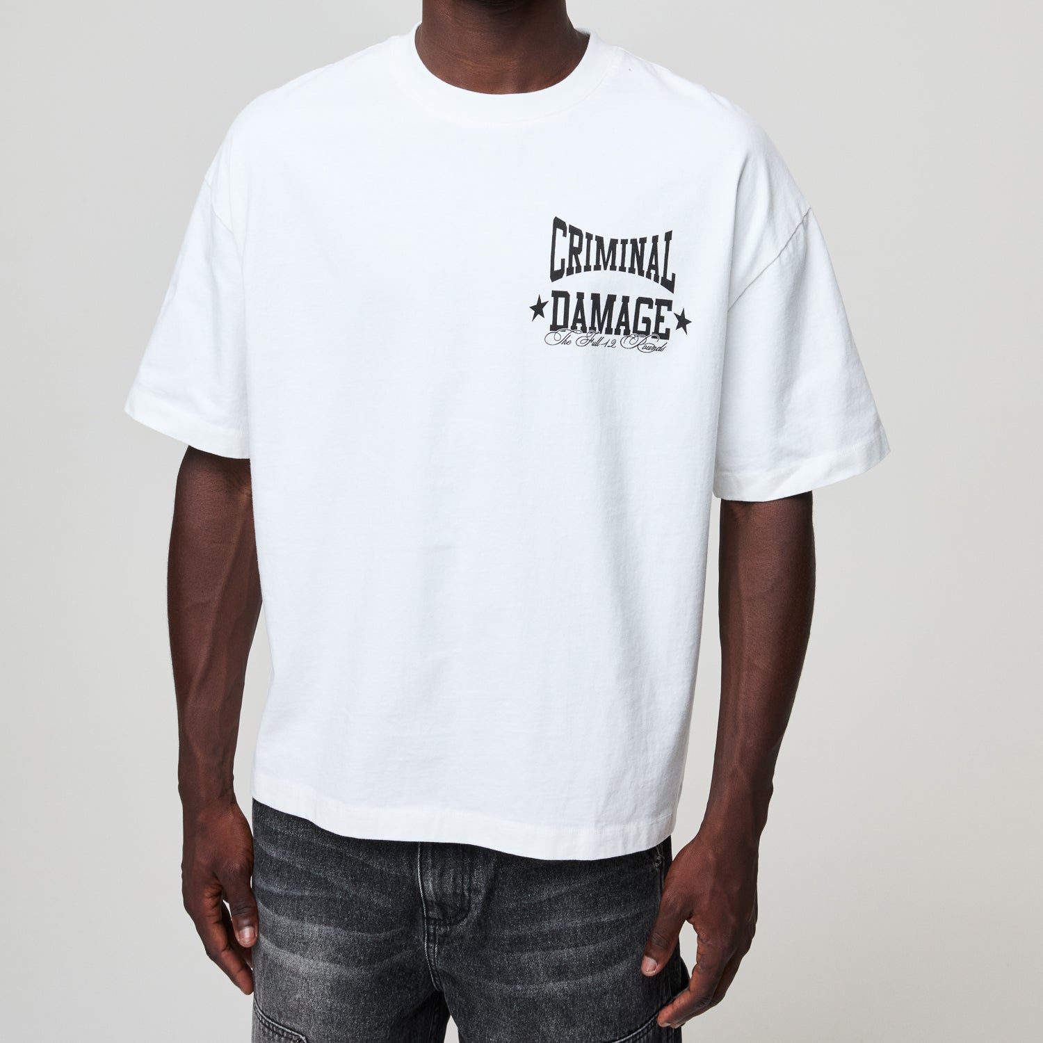 Person wearing a white t-shirt with 'Criminal Damage' print on a plain background