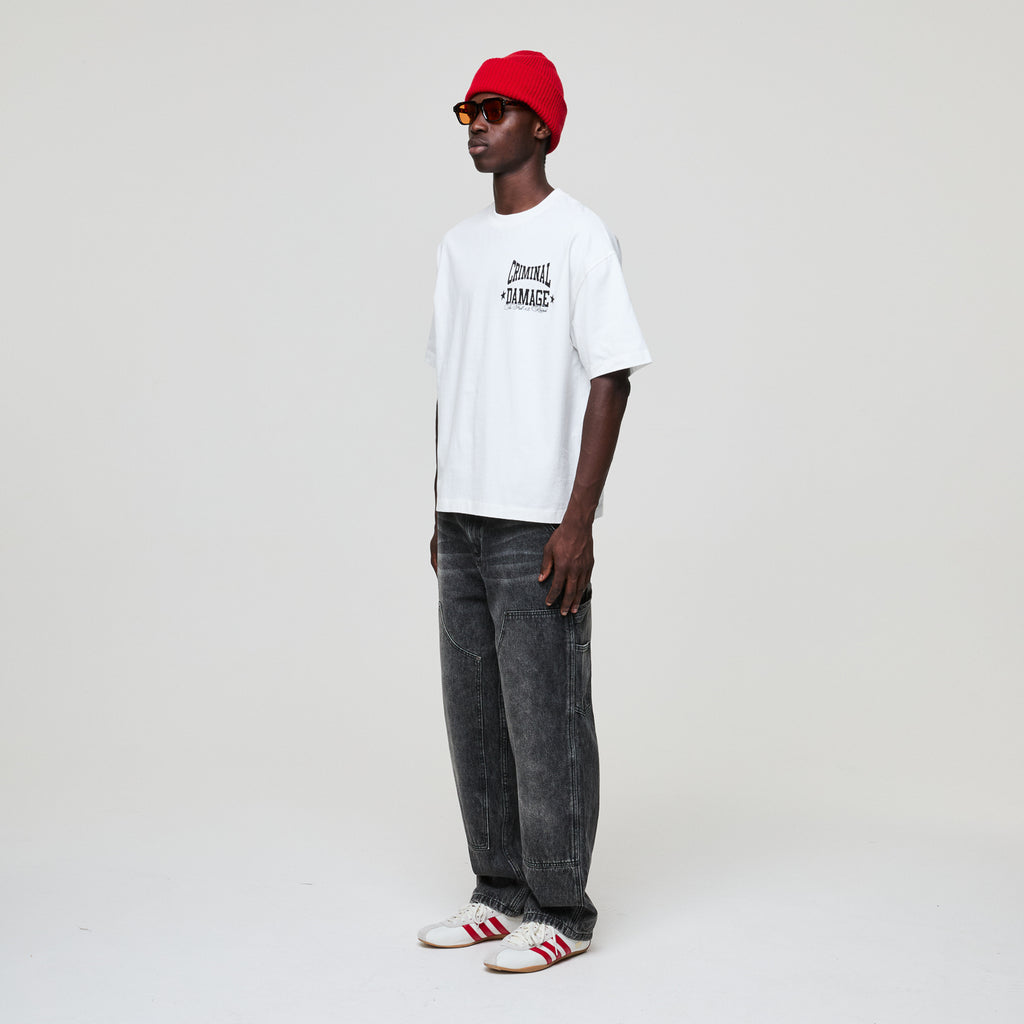 Person wearing a white Criminal Damage t-shirt, red beanie, and gray jeans on a white background