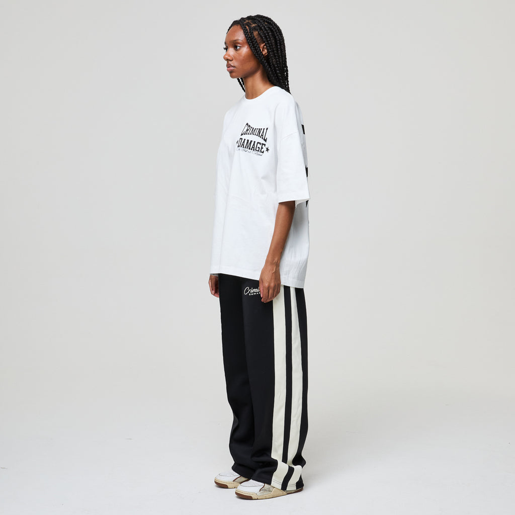 Person wearing a white t-shirt and black pants with white stripes on a plain background