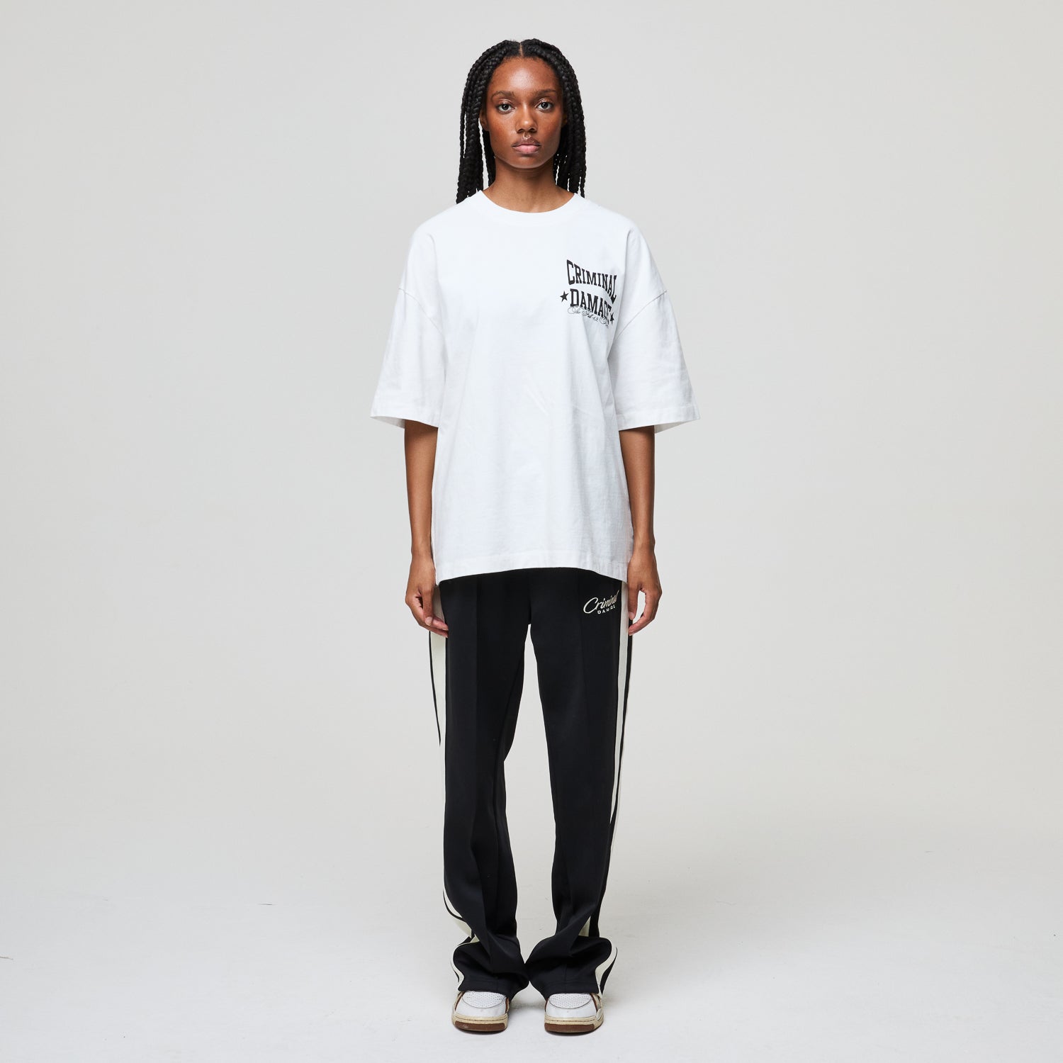 Model wearing a white oversized t-shirt and black pants with stripes on a plain background
