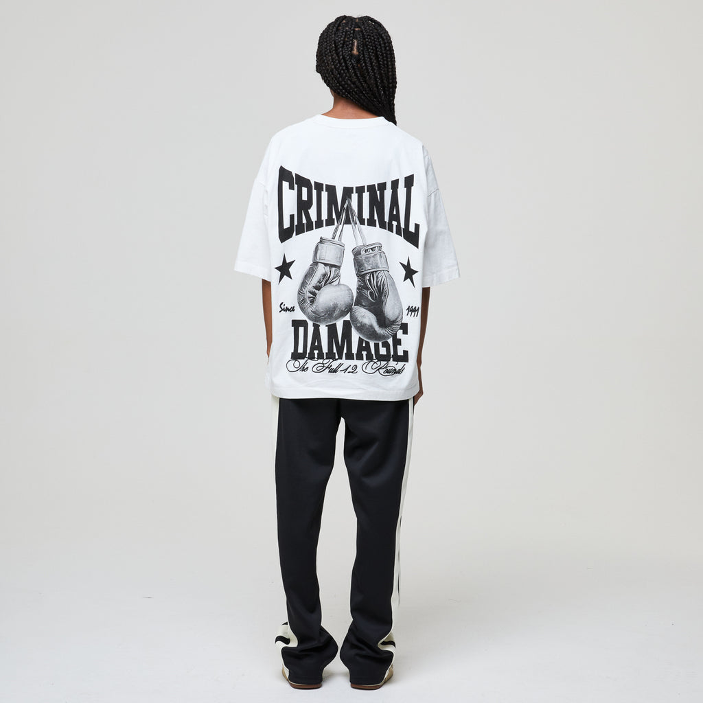 Person wearing a white t-shirt with 'Criminal Damage' text and boxing glove graphics on a plain background