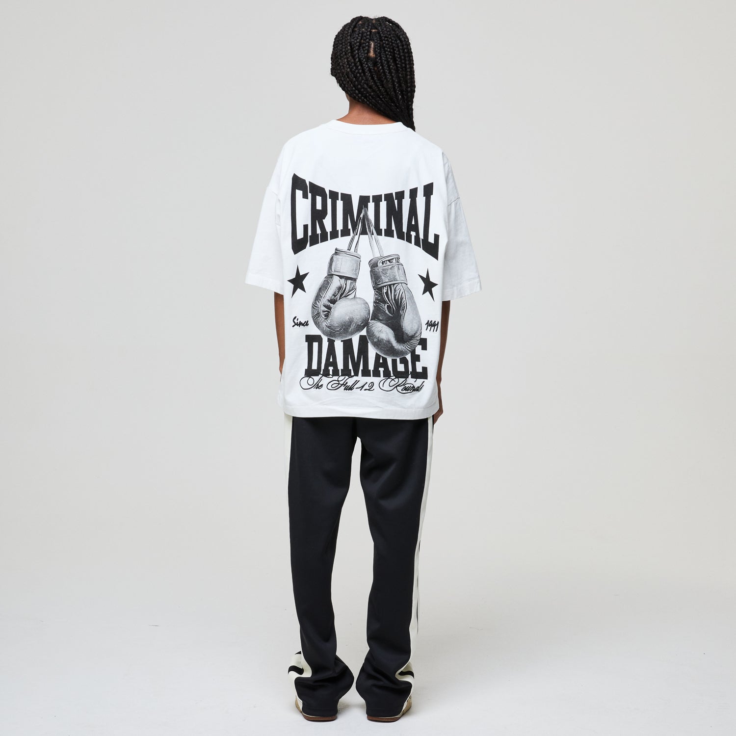 Person wearing a white t-shirt with 'Criminal Damage' text and boxing glove graphics on a plain background