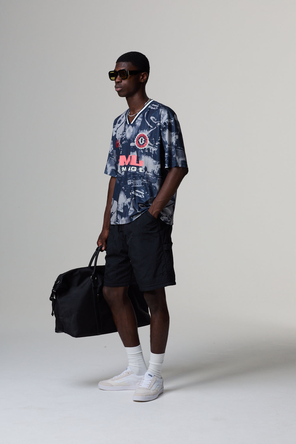 Model wearing a Criminal Damage jersey and black shorts, holding a black bag on a grey background