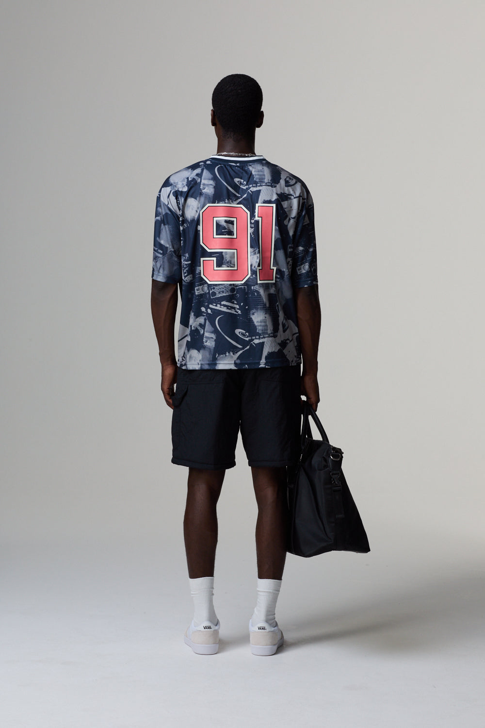 Model wearing a Criminal Damage jersey with the number 91, black shorts, and white shoes on a grey background.