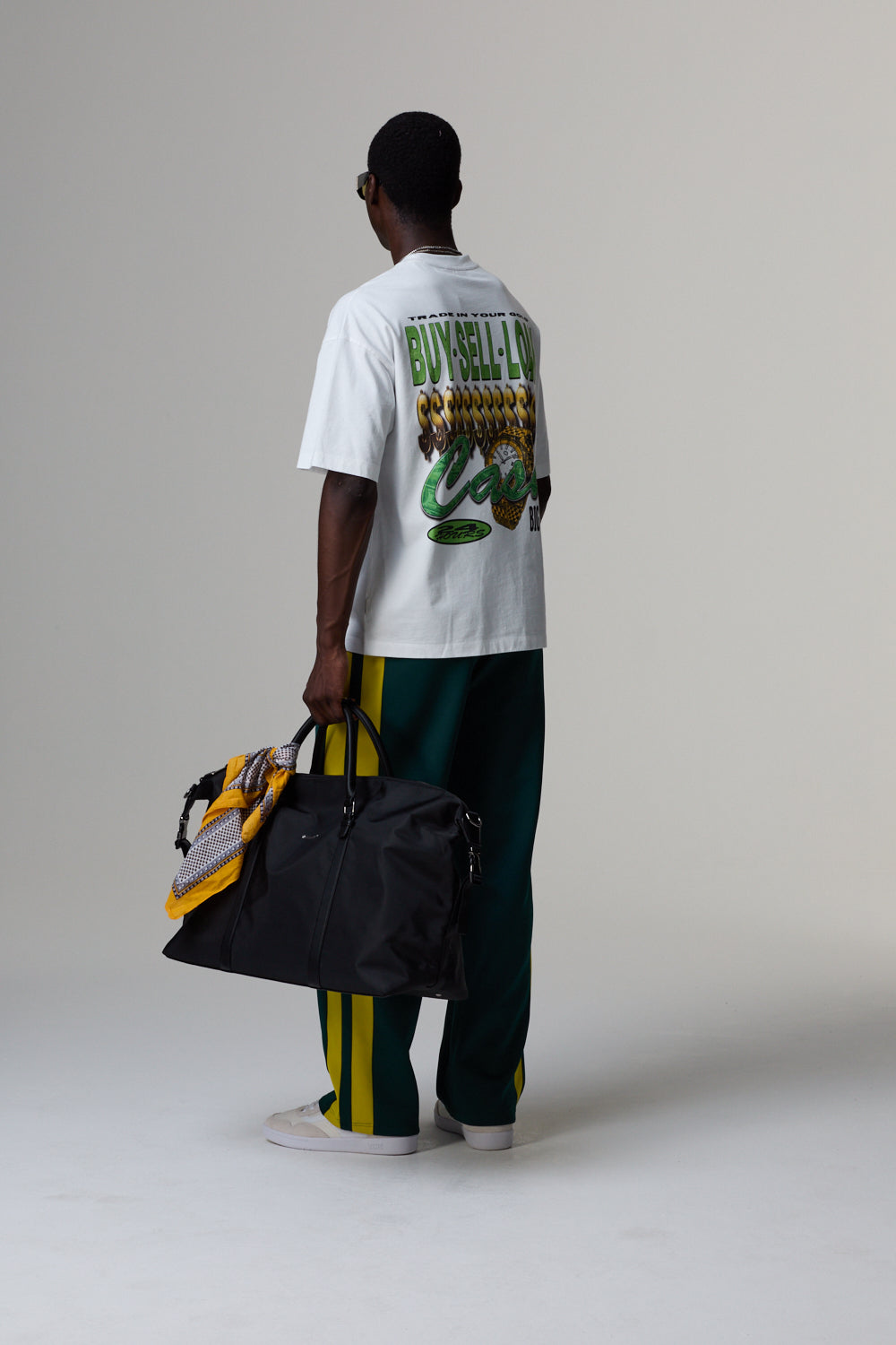 Model wearing a white Criminal Damage t-shirt with text and graphics, holding a black duffel bag on a grey background