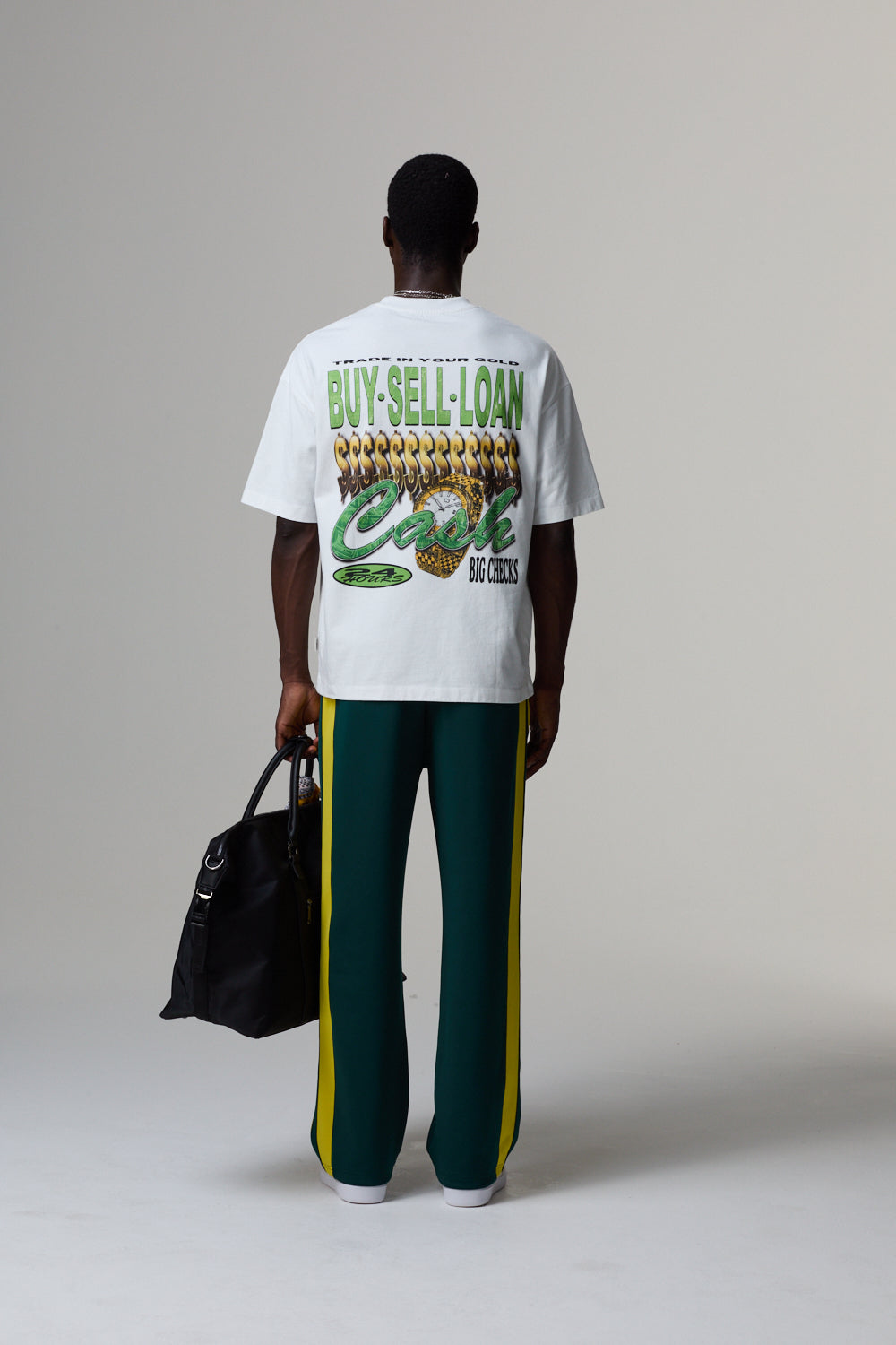 Model wearing a white Criminal Damage t-shirt with graphic design, holding a black bag on a grey background