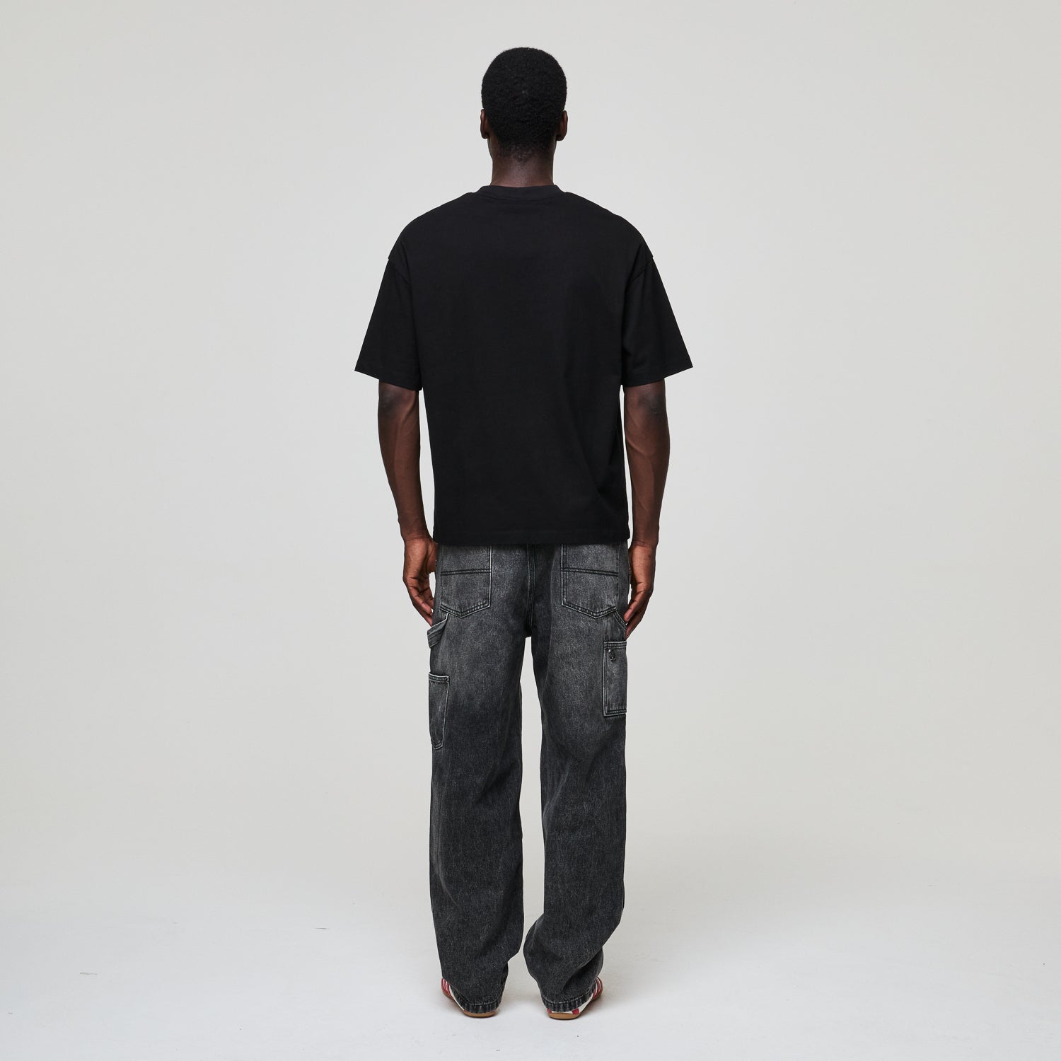 Person wearing a black Criminal Damage t-shirt and gray jeans on a white background