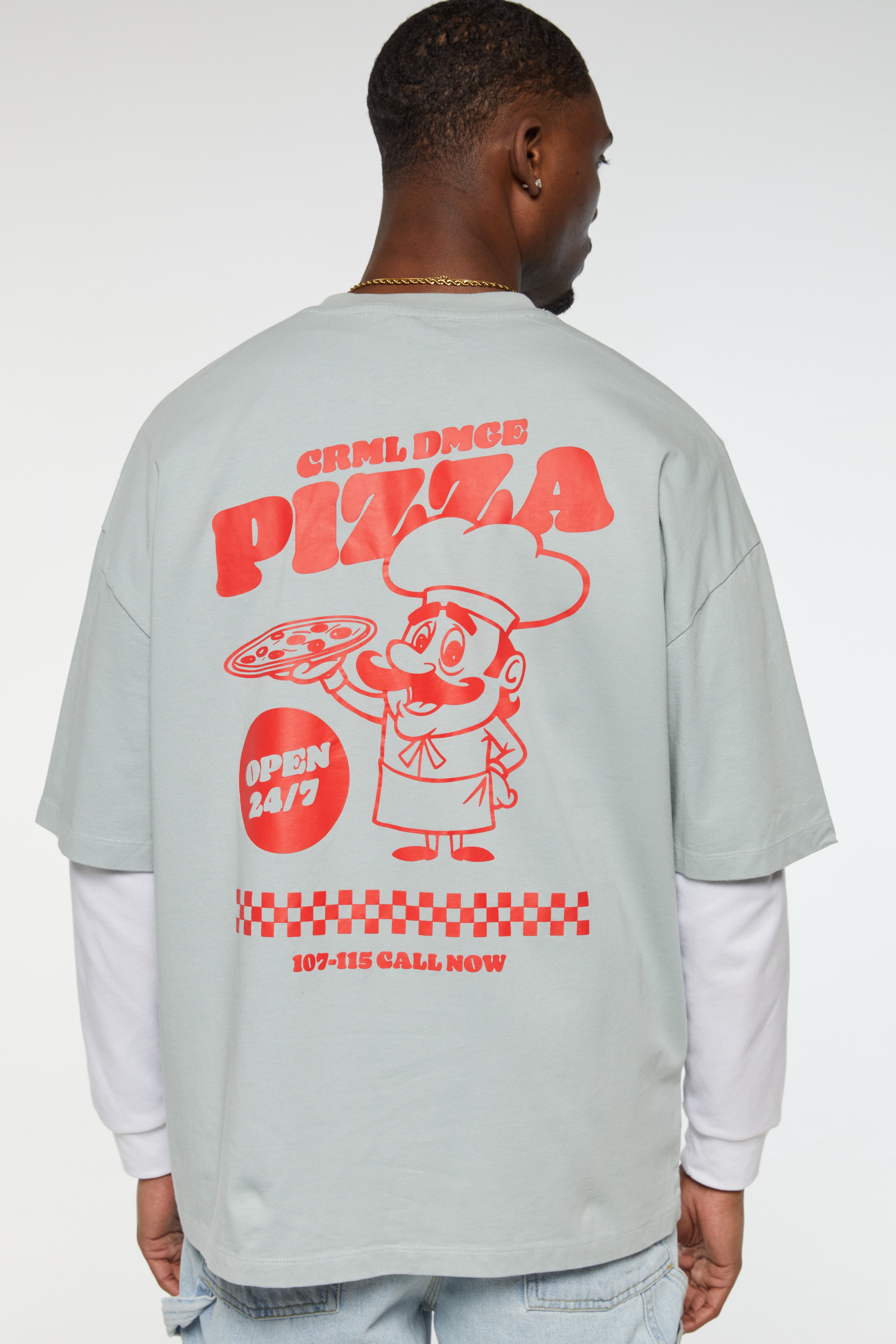 A male model wearing an oversized gray t-shirt with 'GRIL DINE Pizza' text and a pizza character illustration on the front and additional text on the back.