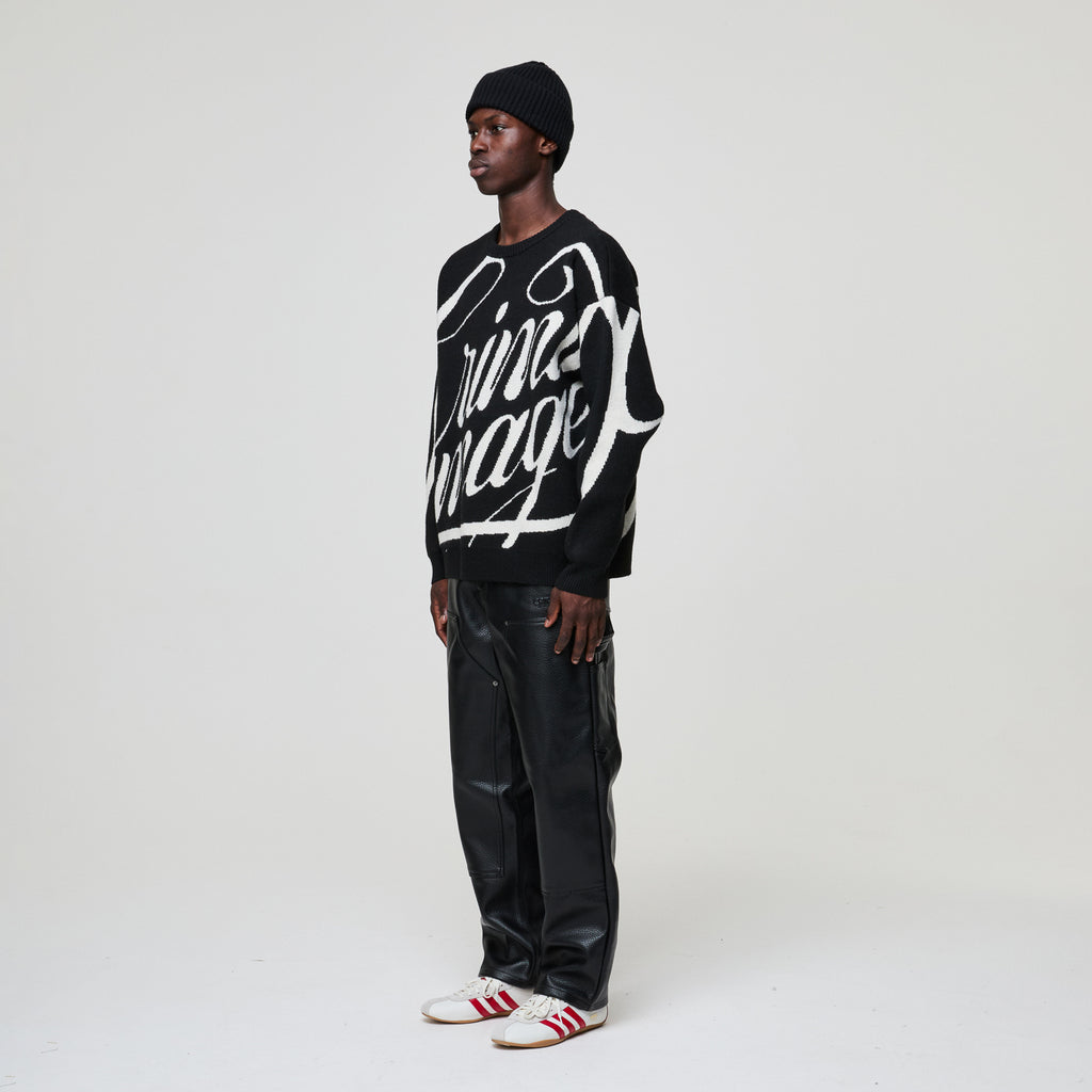 Person wearing a black sweater with white text, black pants, and a black beanie on a white background