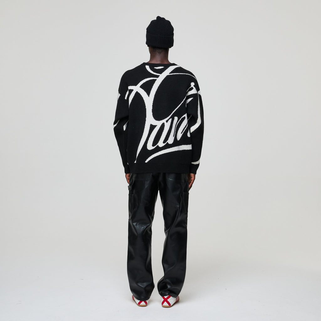 Person wearing a black sweater with white text and black pants on a light gray background