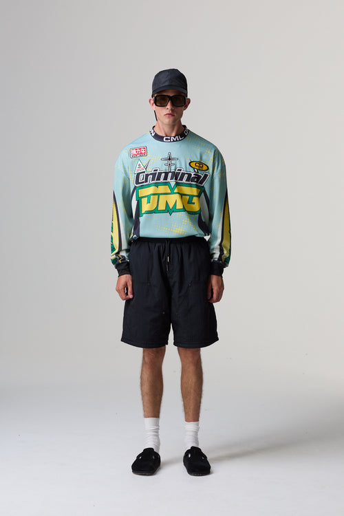 Model wearing a colourful Criminal Damage jersey with brand logos and black shorts on a grey background