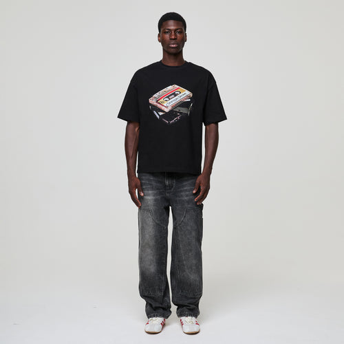 Person wearing a black Criminal Damage  t-shirt with a graphic design on a plain background