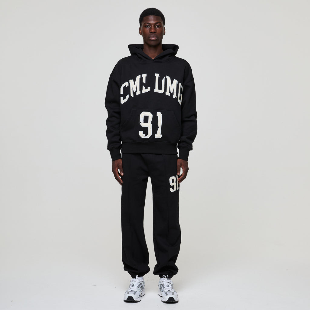 Person wearing a Criminal Damage black hoodie and pants with text and numbers on a white background