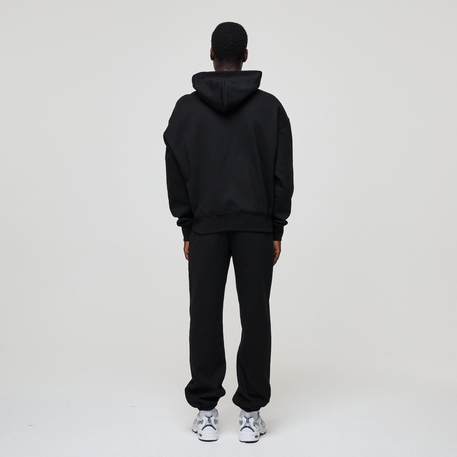 Person wearing a black hoodie and pants set on a white background