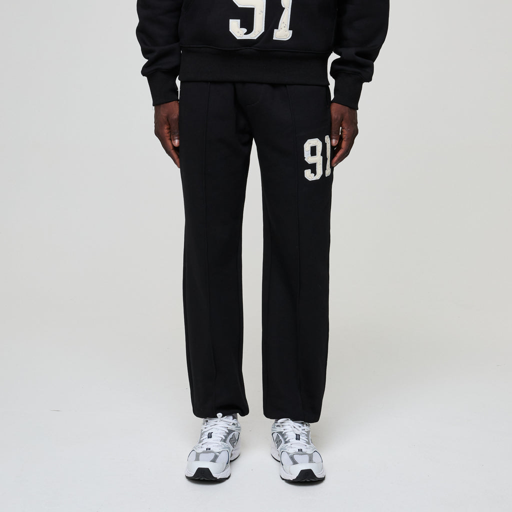 Person wearing a black tracksuit with '91' printed on it against a white background