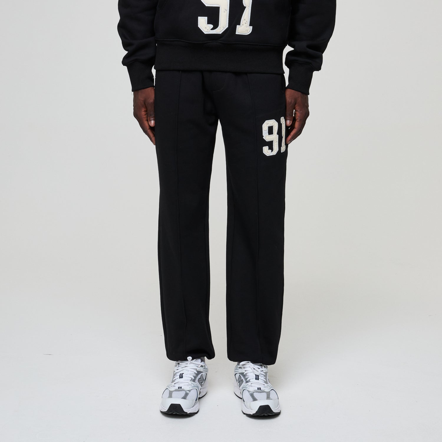 Person wearing a black tracksuit with '91' printed on it against a white background