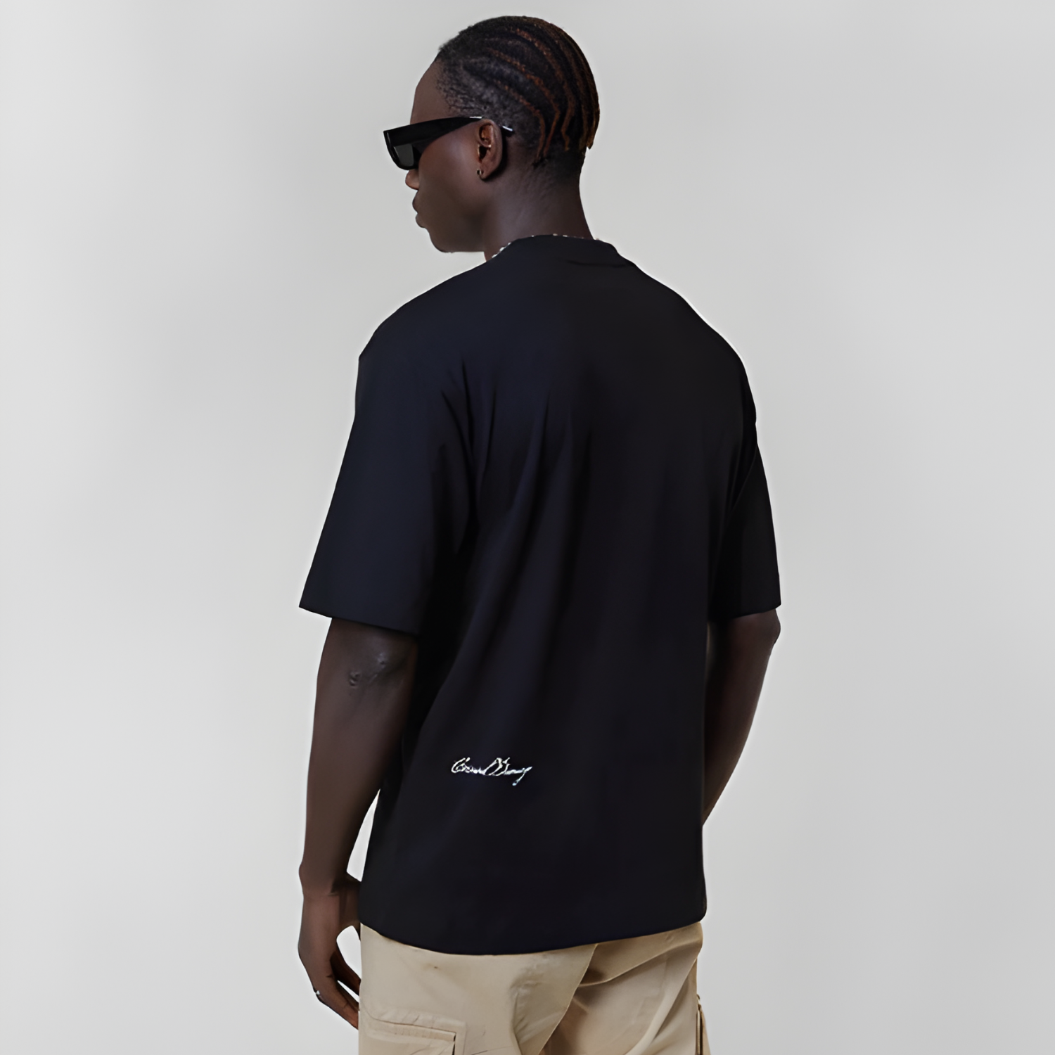 Man wearing a black t-shirt with a logo, sunglasses, and beige pants on a plain background