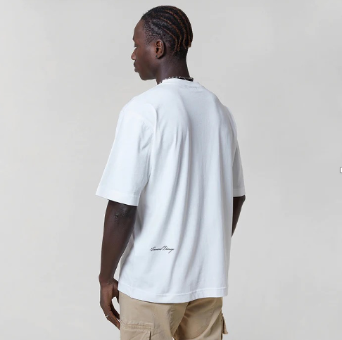 Man wearing a white  t-shirt with a logo, sunglasses, and beige pants on a plain background