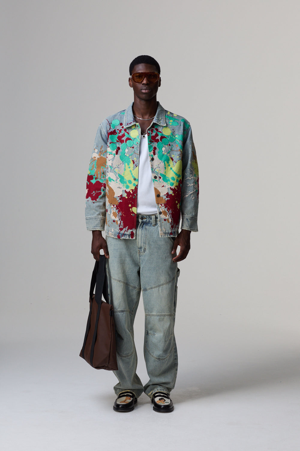 Model wearing a colourful Criminal Damage jacket and light jeans on a grey background