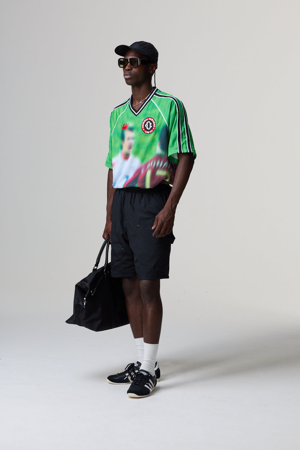 Model wearing a Criminal Damage jersey with a graphic design, holding a black bag on a grey background