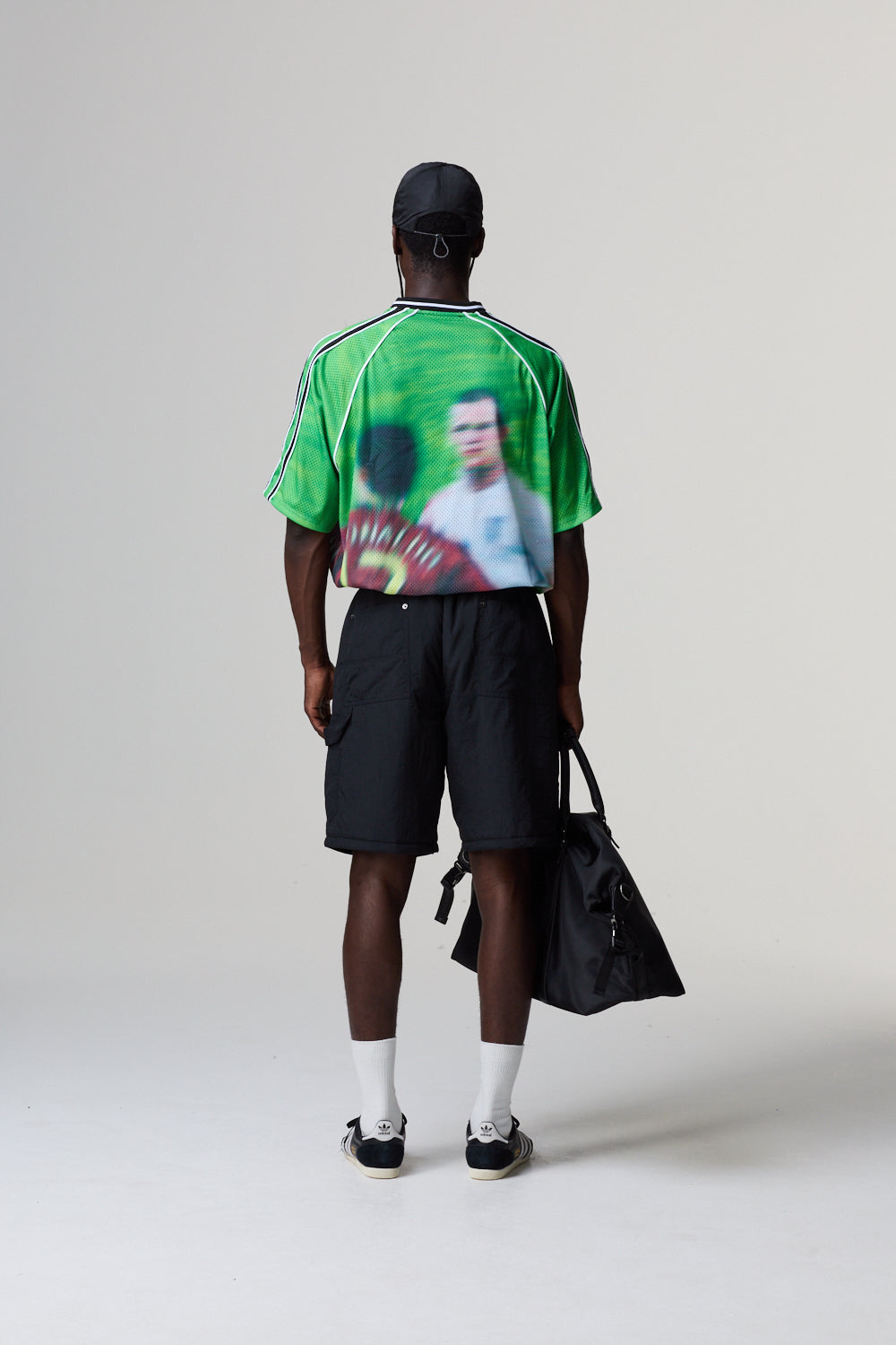 Model wearing a Criminal Damage jersey with a graphic design, holding a black bag on a grey background