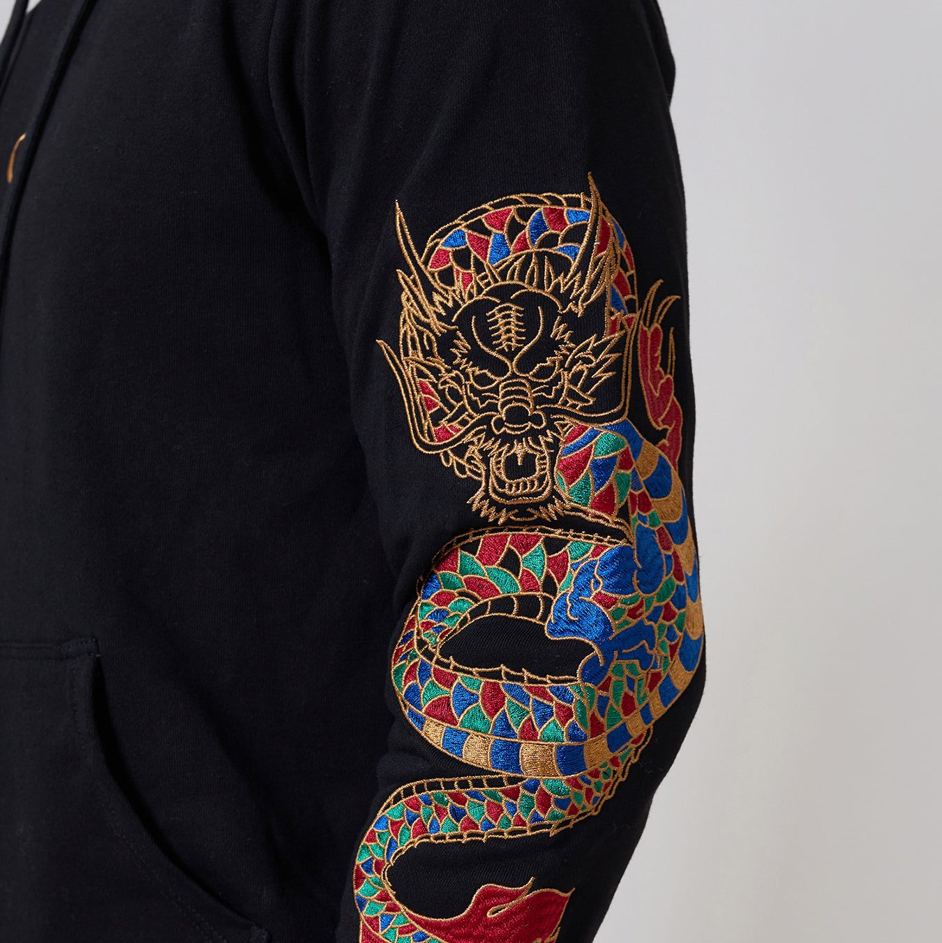 Man wearing a Criminal Damage black hoodie with a colourful design and beige cargo pants on a white background