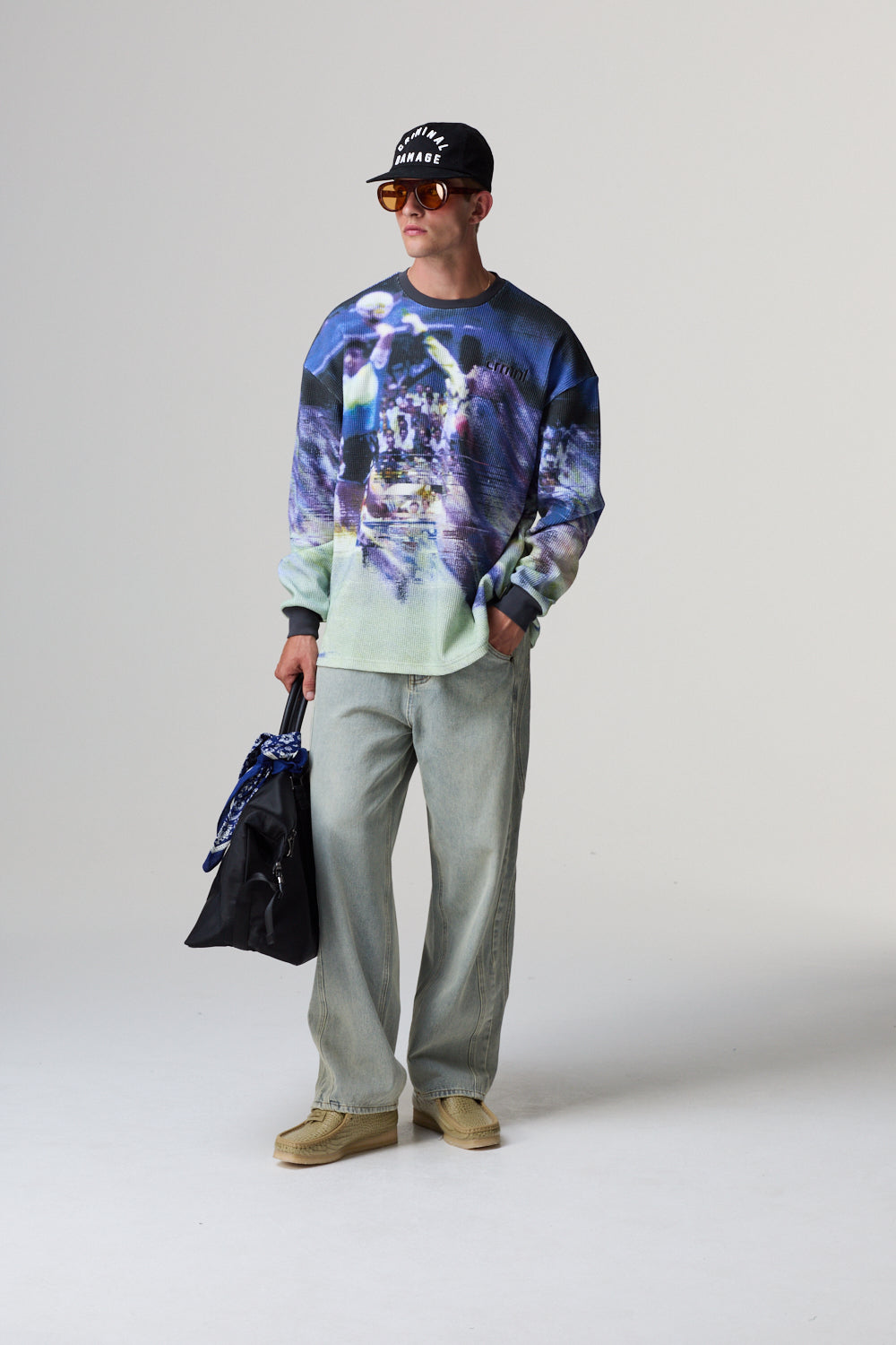 Model wearing a colourful Criminal Damage sweater and holding a black jacket on a plain background