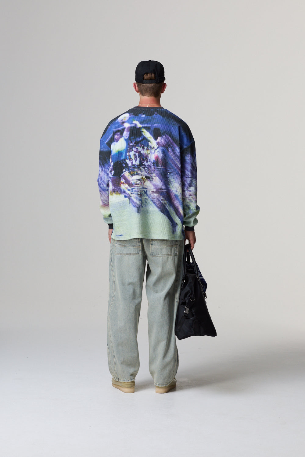 Model wearing a colourful sweater with a graphic design, standing against a plain background