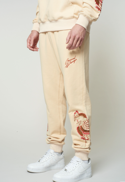 Beige sweatpants with red embroidery and white sneakers on a plain background