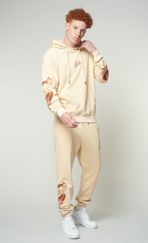 Person wearing a beige tracksuit with floral designs on a plain background