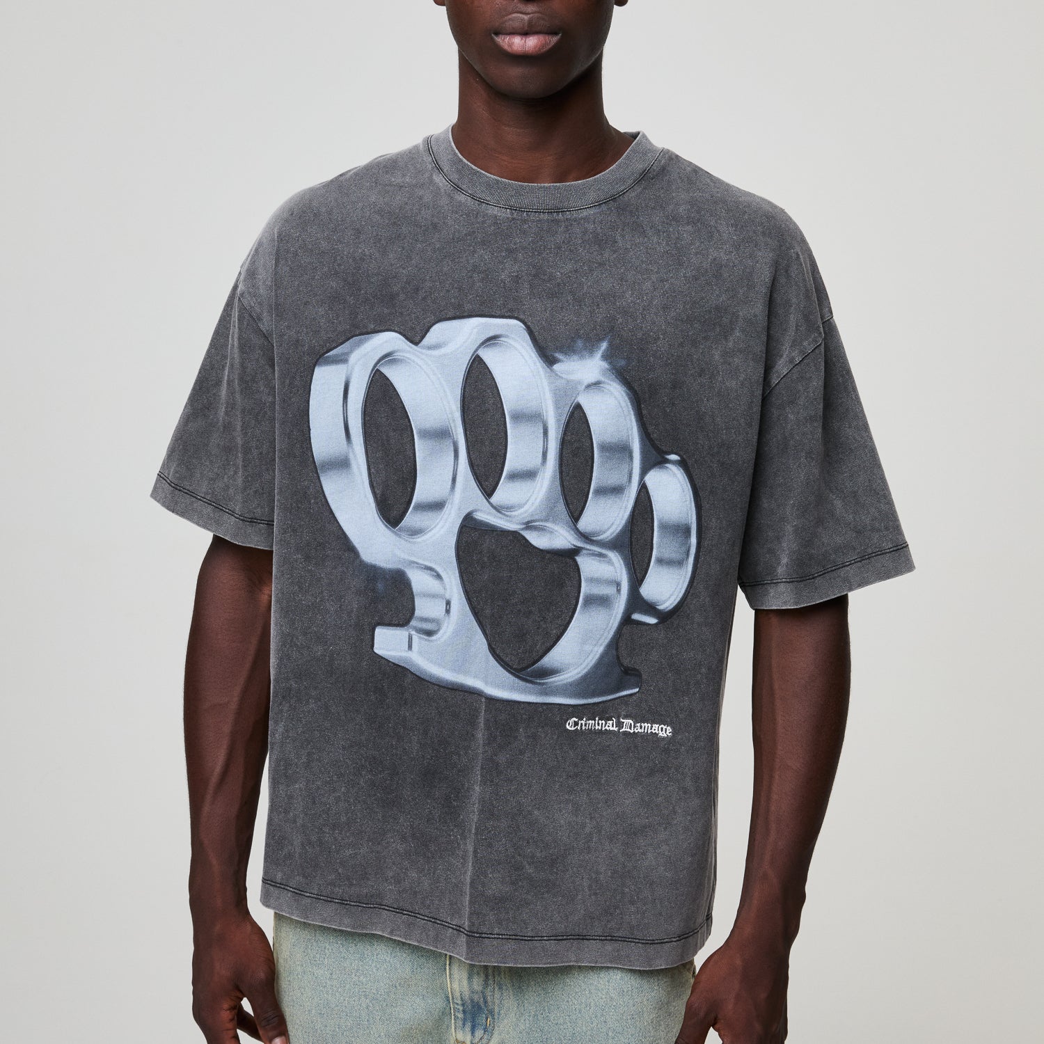 Person wearing a gray Criminal Damage t-shirt with a large graphic design on a plain background