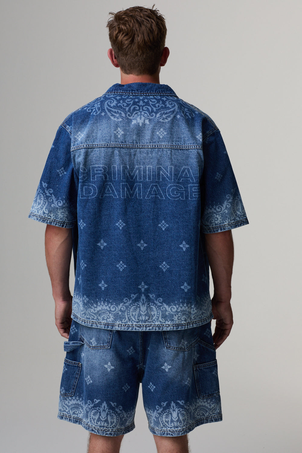 Model wearing a blue denim Criminal Damage shirt and shorts on a grey background
