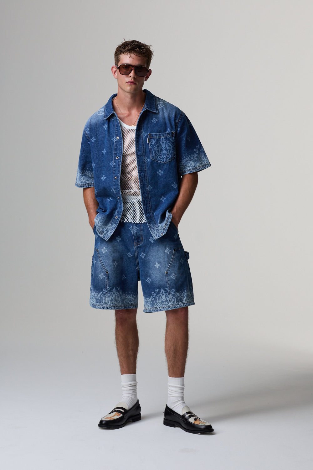 Man wearing a blue Criminal Damage denim outfit with sunglasses on a grey background