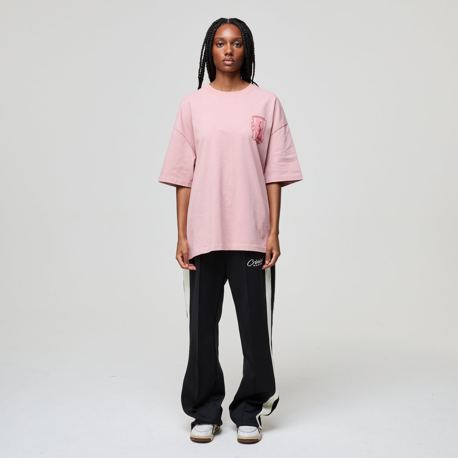 Person wearing a pink oversized t-shirt and black pants with white stripes on a plain background