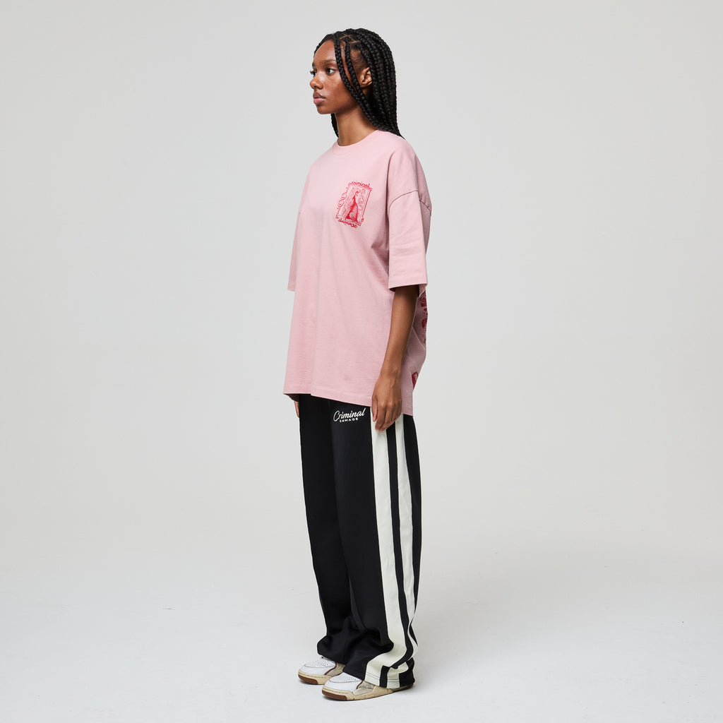 Person wearing a pink oversized t-shirt and black and white striped pants on a plain background