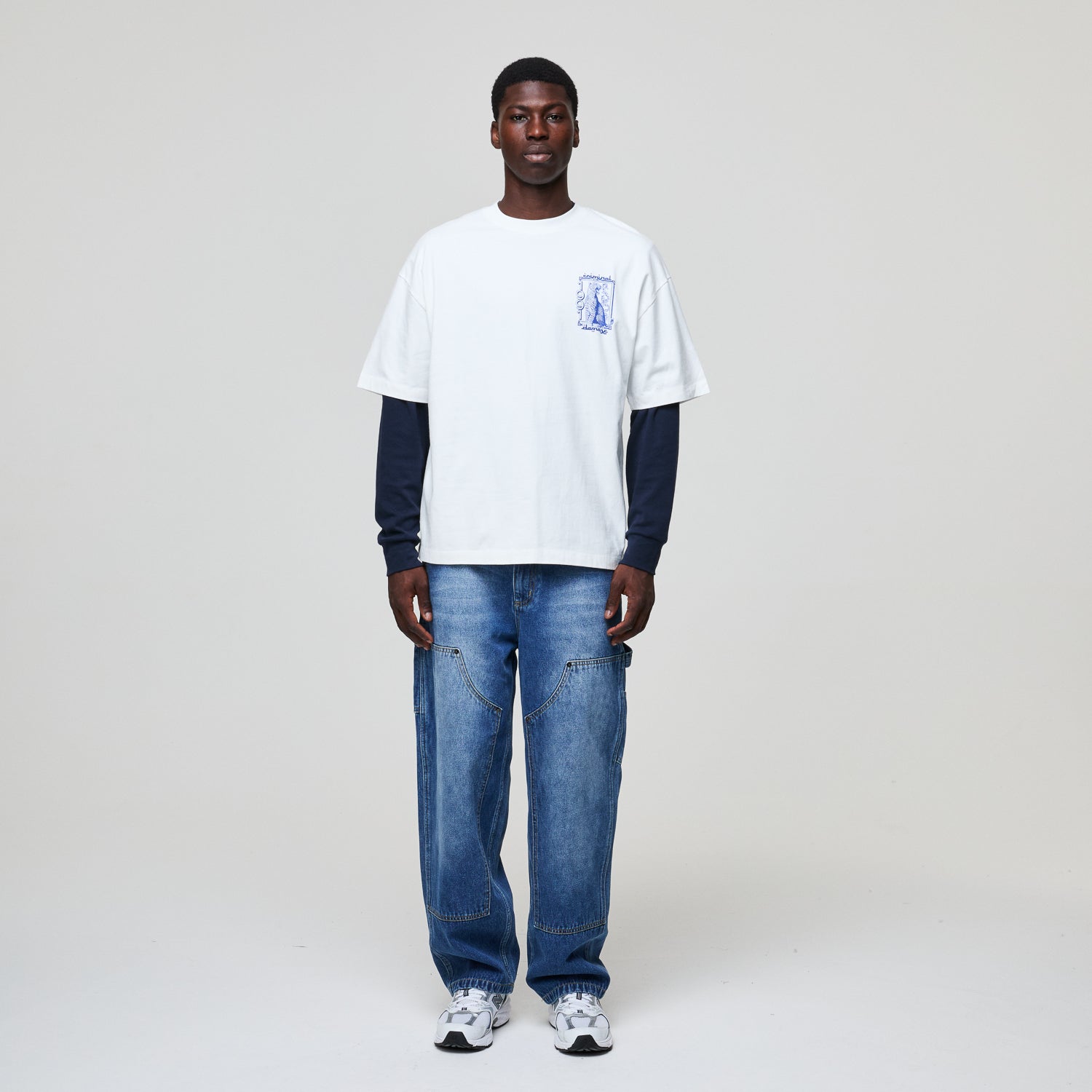 Person wearing a white t-shirt with a logo and blue jeans on a plain background