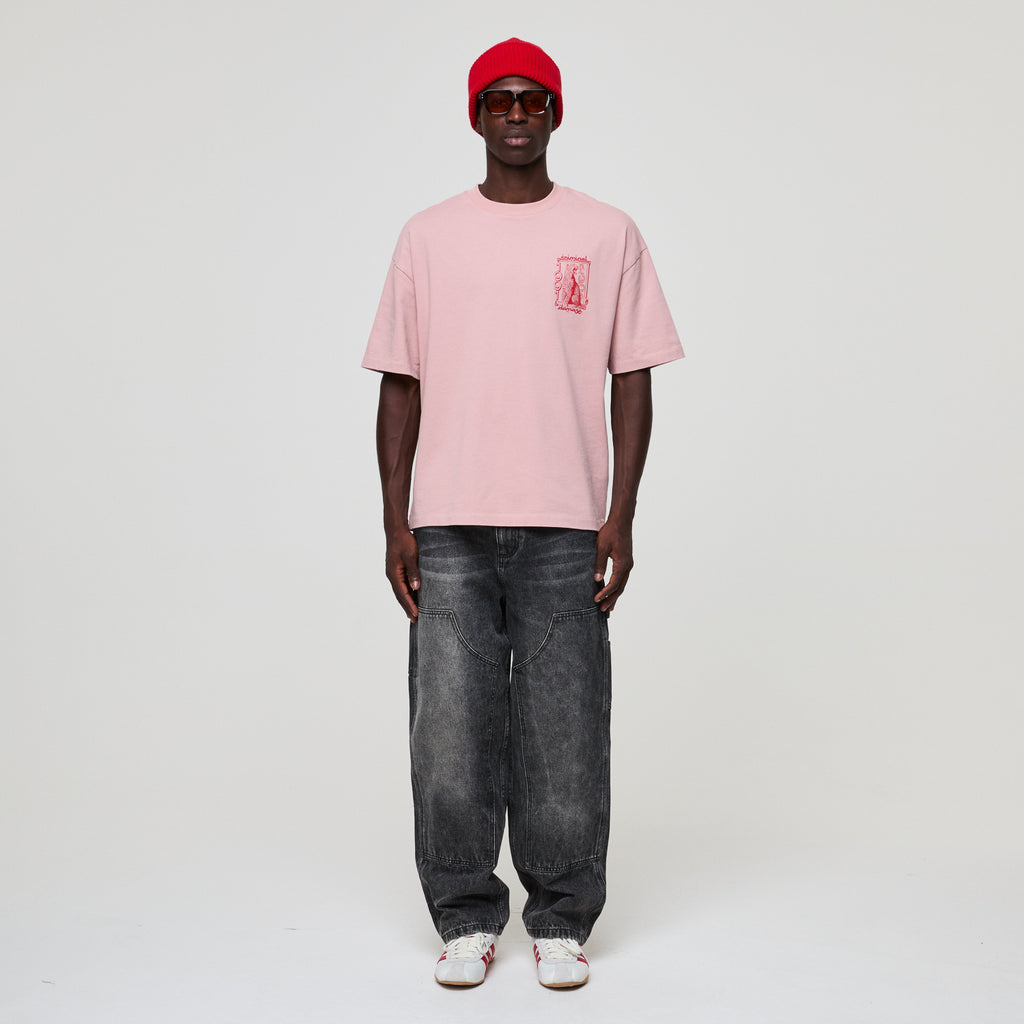Person wearing a pink t-shirt with a logo, black jeans, and a red cap on a white background